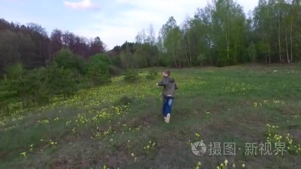 跑过草地在森林里的小男孩。那个男孩有一个好心情。草坪的点缀着黄色的花朵。春天的一天晚上在森林里