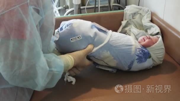 护士在手套缠着铭牌上桌上出生后裹着刚出生的婴儿。妇产科医院
