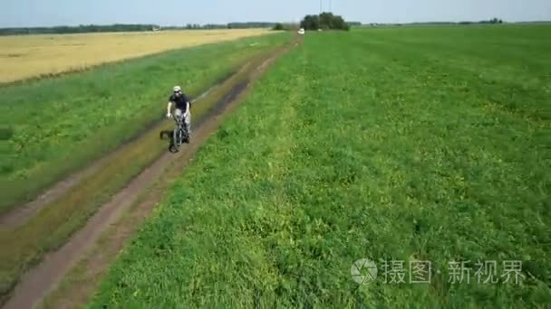 空中 ︰ 年轻人骑自行车在农村公路通过绿色和黄色字段