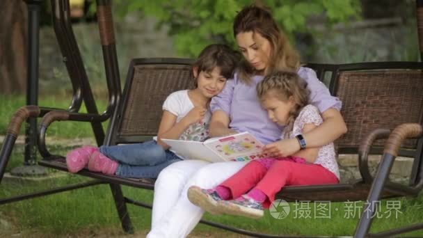 母亲给孩子坐在公园里读一本书视频