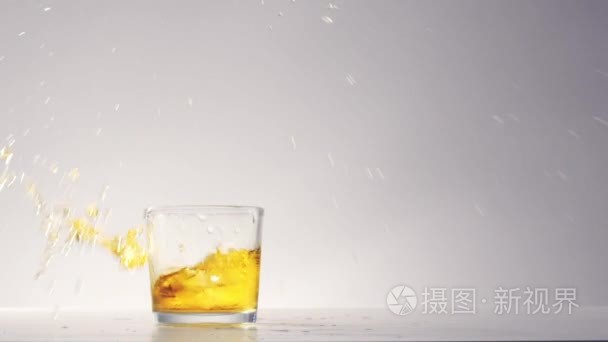 big ice cube falls into glass with yellow drink 