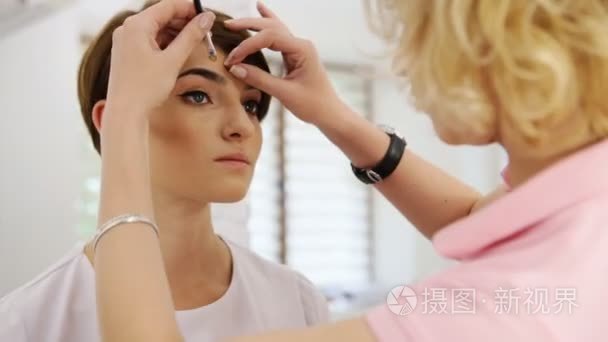 美丽的女人绘图使用眉笔的眉毛形状。化装师应用对模型进行视频