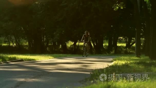 女人开始骑着单车穿过绿色的草地公园树木和日落