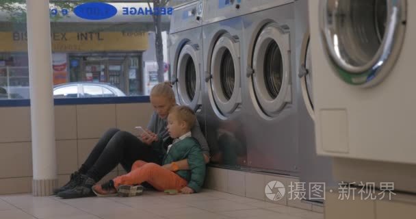 母亲和儿童使用手机在洗衣房视频
