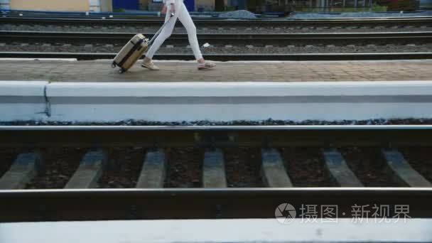 一个女人穿着商务装在一个旅行袋是火车站。在图片中可以看到只有腿部和一袋车轮上