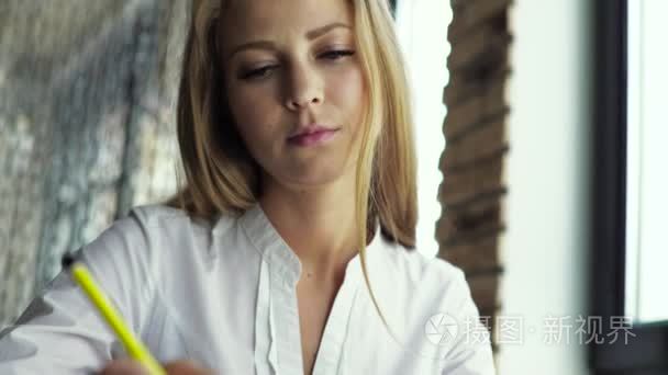 Blonde woman sitting at the table, writing in the notebook and d