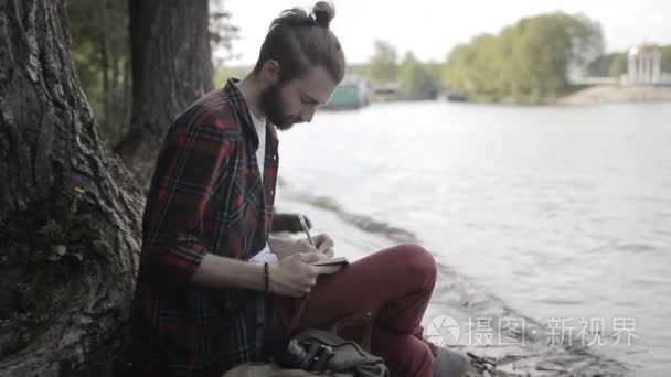 男人坐在岸边的笔记本中记笔记视频