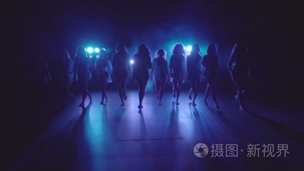 Shilouettes of female dancers group sensually walking on a dark 