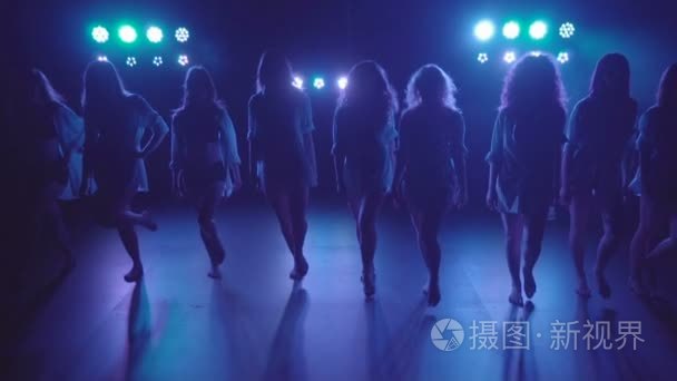 Shilouettes of female dancers group sensually walking on a dark 