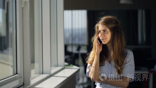 Young woman talking on phone in office looking out window  her h