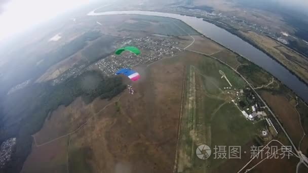 与彩色降落伞平衡在绿色的田野上空跳伞。河
