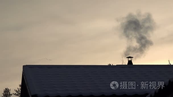 鸟飞落日的冬天的晚上，那烟从烟囱上被雪覆盖的屋顶的房子