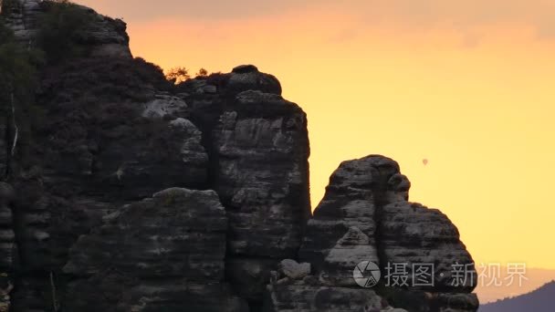 热气球 （大气气球） 飞翔在天空，隐藏在岩石尖峰。傍晚日落山景观、 橙色的天空和高湿度的空气