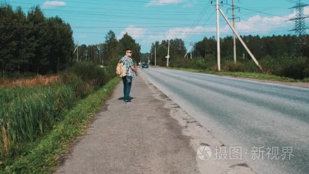 Boy with backpack walking along roadside. Hitchhiking. Traveler.