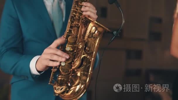 Saxophonist in blue suit play jazz on golden saxophone on stage.