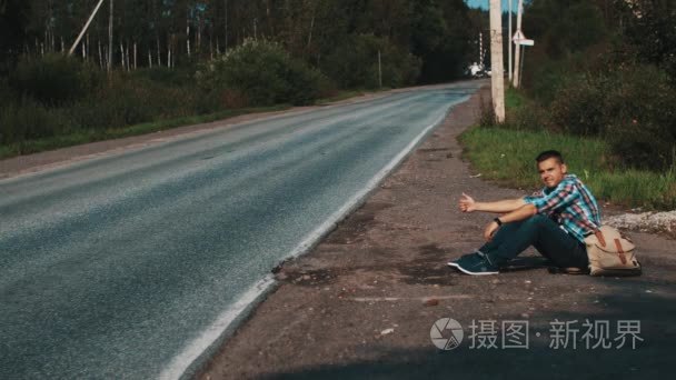 坐在农村道路，背包里的人。搭便车。大拇指。旅行