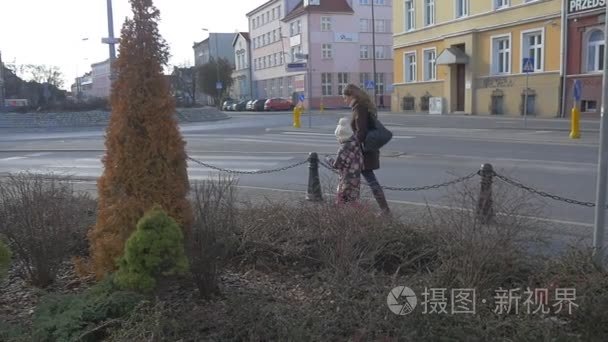 女人和孩子绕过路上的干草坪由街道市容奥波莱行人走在人行道上旧建筑装饰常青树