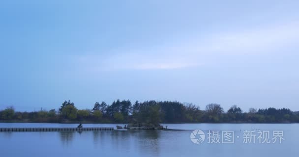 Man Sits Down on Wooden Pier on River Small Island Overgrown Wit