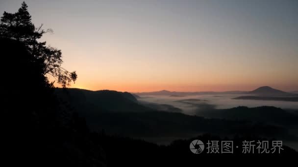 在秋天在丘陵景观天亮前的最后时刻。山峰增加从橙色和粉红色的雾海。时间流逝