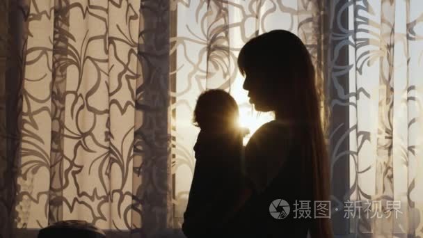 silhouette of a young mother with a child at the window. Swaying