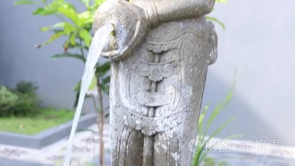 Asian balinese stone statue of woman with jug. The water flowing