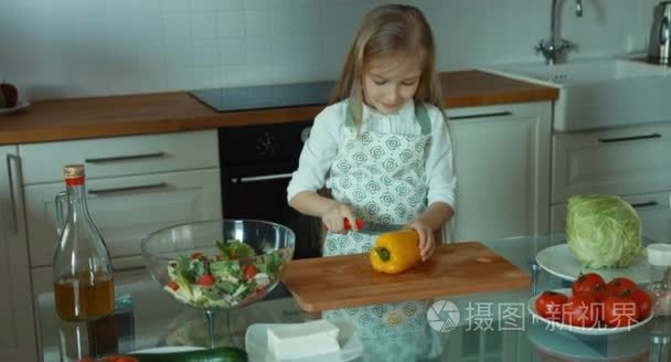 切辣椒的女孩。儿童厨师在厨房里看着相机和微笑