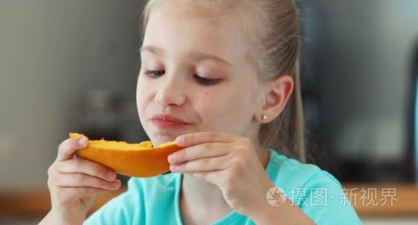 特写肖像女孩吃芒果。孩子坐在餐桌旁，看着相机