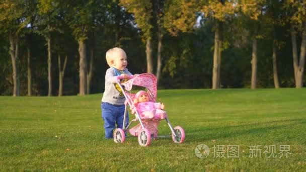 小男孩站在一辆粉红色的婴儿车公园