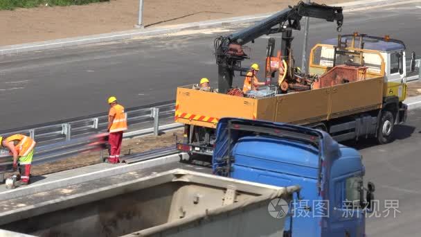 工人男队在新公路道路建设上装载安全栅栏