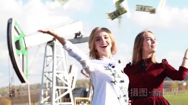 两个年轻快乐妇女扔美元为背景，在油田集输油泵