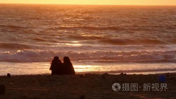 在日落时分坐在海滩上的两个女性