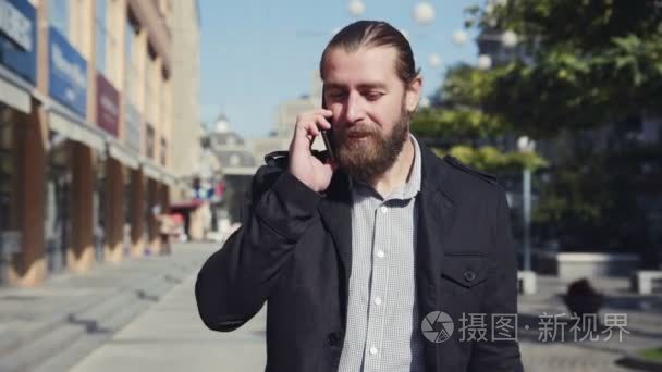 有胡子的人走在城市的街道和用电话交谈