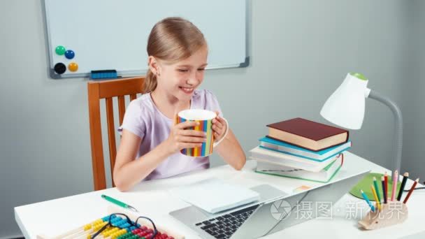 肖像快乐女生 7-8 年捧着杯茶看着笔记本电脑和微笑与相机的牙齿