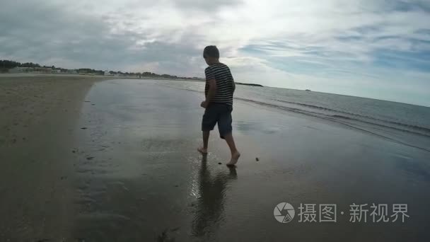 伤心的男孩在湿湿的沙地上行走