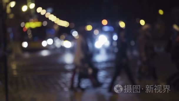 慢动作镜头的夜交通在城市的中心。行人在人行横道过马路。模糊的图像的过路的人