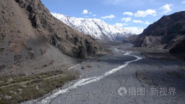 窄窄的山流在群山之间的一个宽阔的山谷中。在远处白雪覆盖的山脉。格鲁吉亚