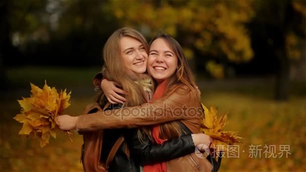 两个美丽少女拥抱，在秋天的公园里，抱着一束黄色的叶子在户外玩乐的女朋友