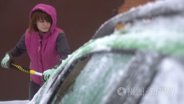 清洗掉她的车冰雪的年轻女人。冬季暴风雪