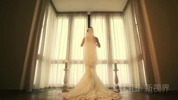 新娘穿着婚纱背面来到窗前，发现白色的窗帘。温暖的色调