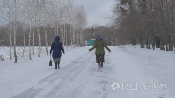 两个女人道灰色的天空多云冬季雪天在户外，而且两边匆匆步行的雪覆盖的道路光秃秃的树木