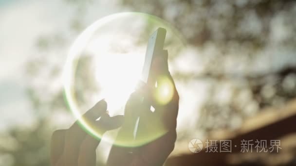 女人手智能手机在日落时的剪影视频