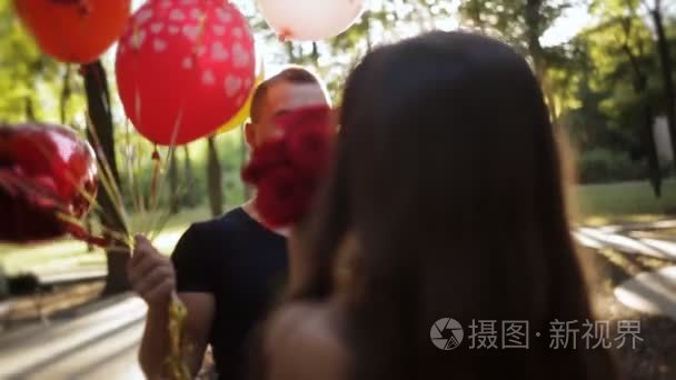 一个家伙走到他的女朋友，一束鲜花和气球进行。女朋友的生日。女孩高兴地跳着，抱着他心爱的人视频
