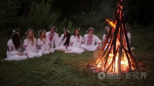 仲夏夜。坐在篝火旁边的斯拉夫衣服的年轻人