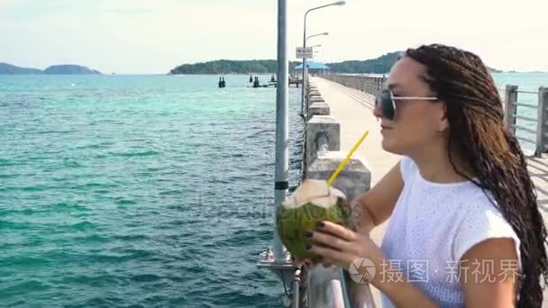 漂亮的女人喝椰子牛奶在码头上视频