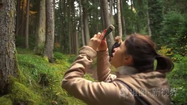 一名年轻女子在美丽的森林，用智能手机慢动作拍张照片