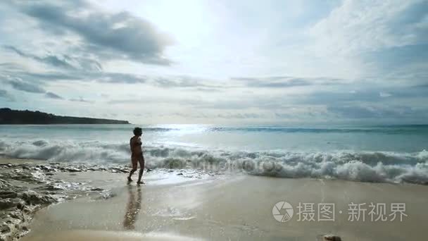 纤细的女孩滚大浪的海洋沿岸沙质海滩上散步。年轻女子几乎撞腿与水