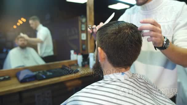 年轻英俊理发师制作的漂亮胡子的男子，在理发店理发