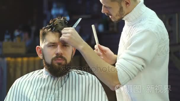 年轻英俊理发师制作的漂亮胡子的男子，在理发店理发