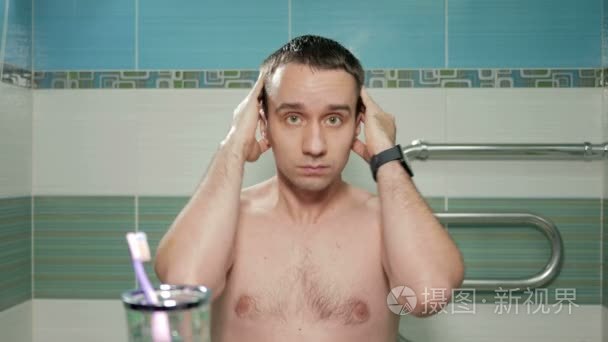 年轻有魅力的男人经过在旅馆房间的浴室里洗个澡之后就直发型。他手梳理头发中所需的方向。他正看着镜子里的相机