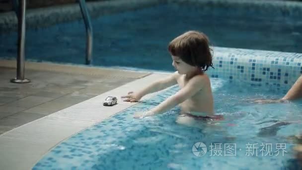 年轻的父母带着儿子在游泳池玩视频